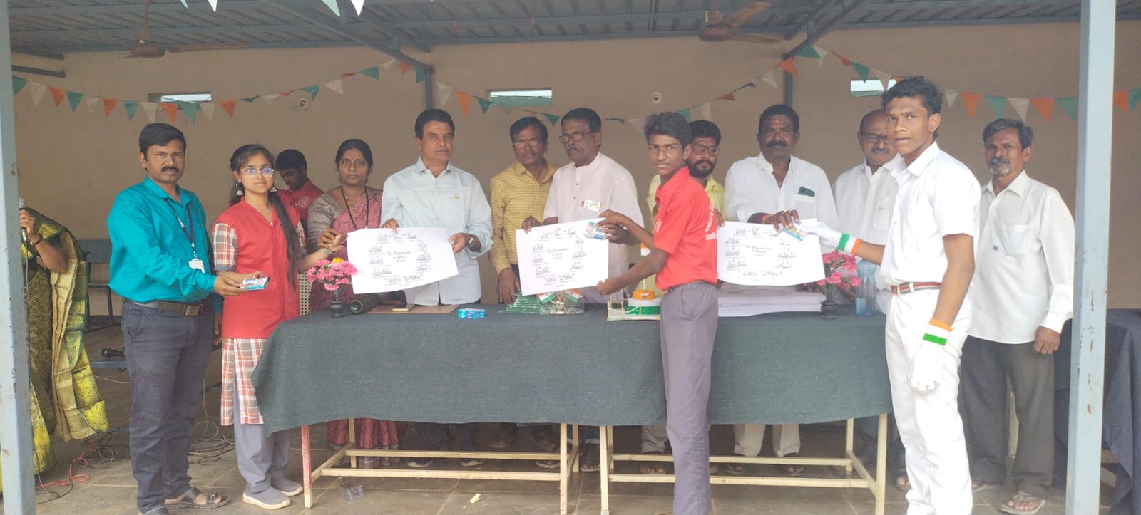 Three students hold up E-Waste Cycle posters in front of officials at a school event in India.